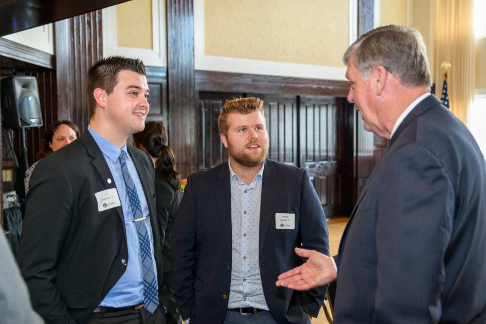 Two male alumni chat with President Haas